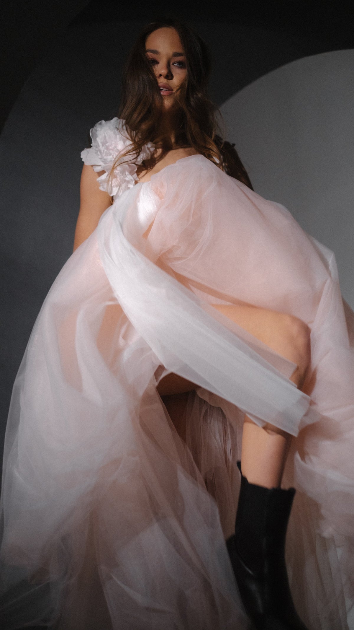 Model kicking up a blush tulle wedding dress skirt to show black boots, silk flower at the shoulder, Chrysanthemum