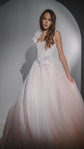 Front view of a blush wedding dress with dropped corset bodice and a silk flower at the hip, model in a pale arch, Chrysanthemum