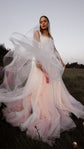 Bride in a blush pink tulle wedding dress lifting a sheer veil in the wind at dusk, lupines in the field behind, Chrysanthemum