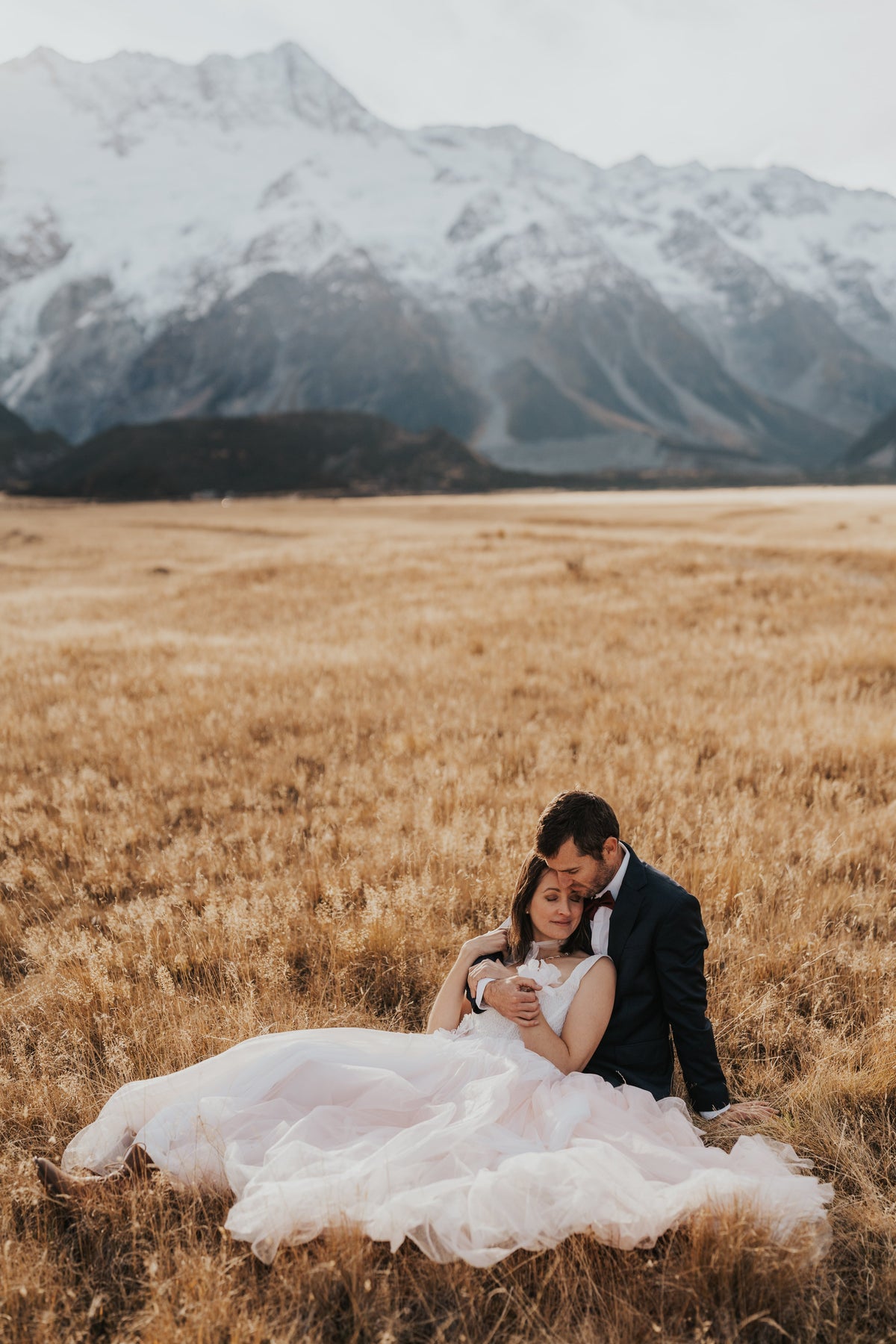 Couple sitting in a wide mountain meadow, blush tulle wedding dress spread across the dry grass, Chrysanthemum