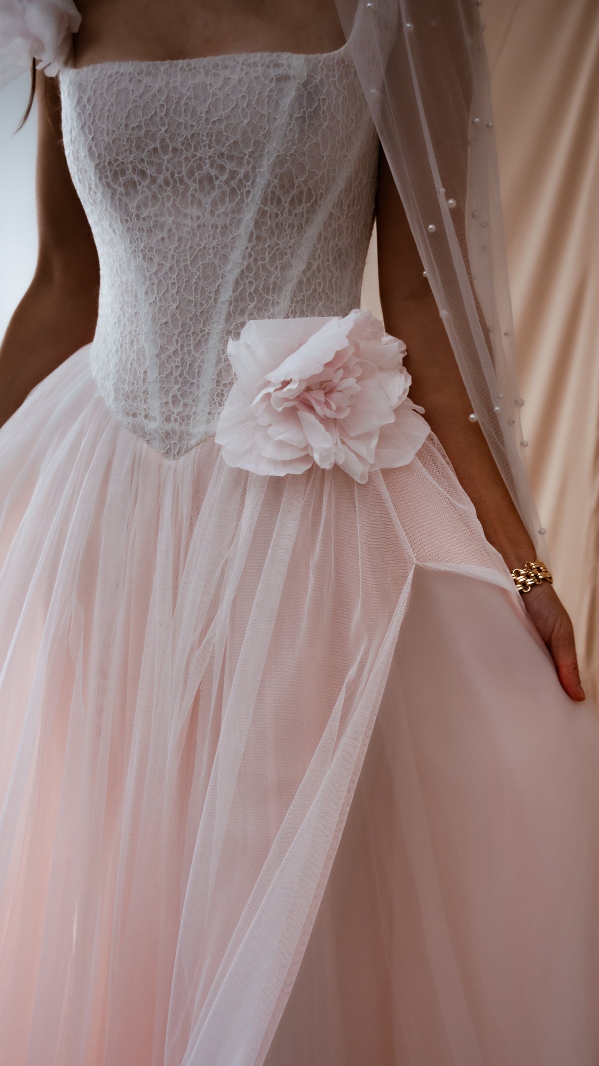 Close-up of a lace corset bodice and silk flower on a blush tulle wedding dress, pearl veil edge at the side, Chrysanthemum