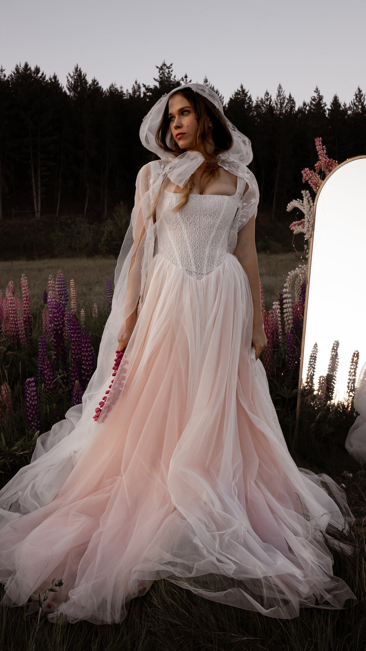Full-length blush wedding dress with a sheer hooded star cape, bride by a mirror in a lupine meadow at dusk, Chrysanthemum