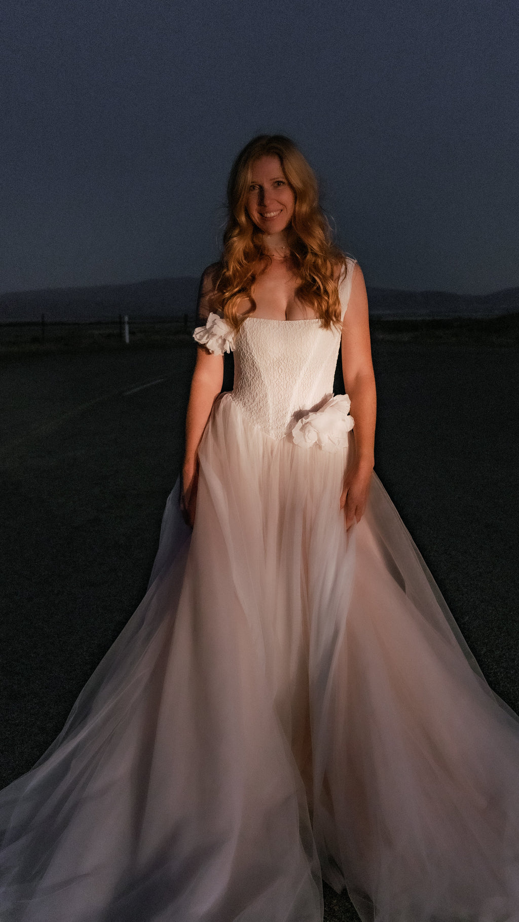 Smiling bride at night in a blush basque waist wedding dress with silk flowers, tulle skirt glowing in the flash, Chrysanthemum