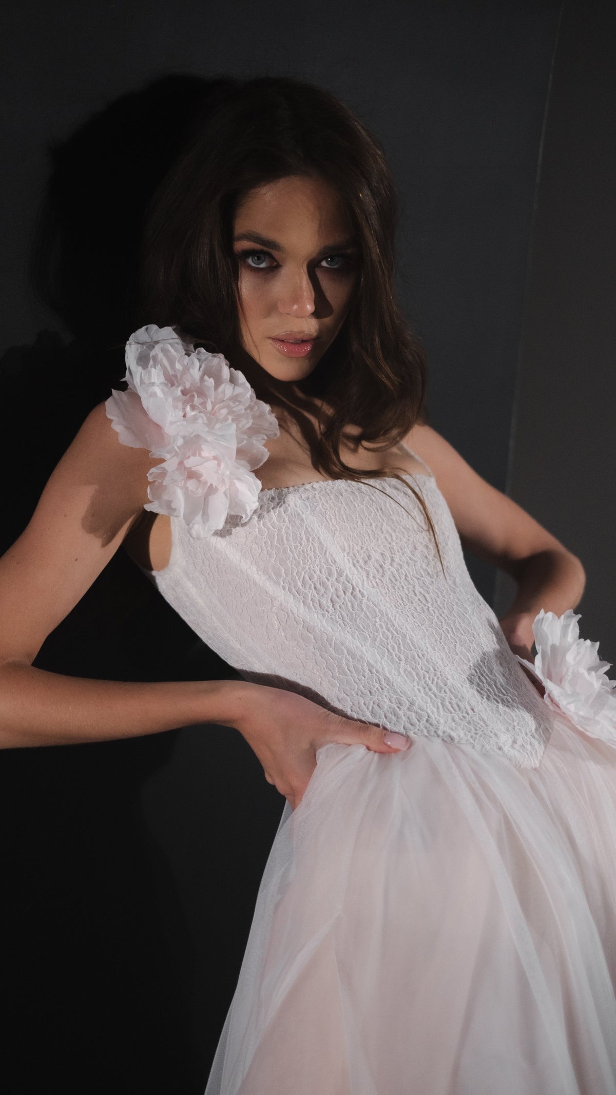 Waist-up view of a lace corset wedding dress bodice with silk flower straps, model leaning in low dramatic light, Chrysanthemum