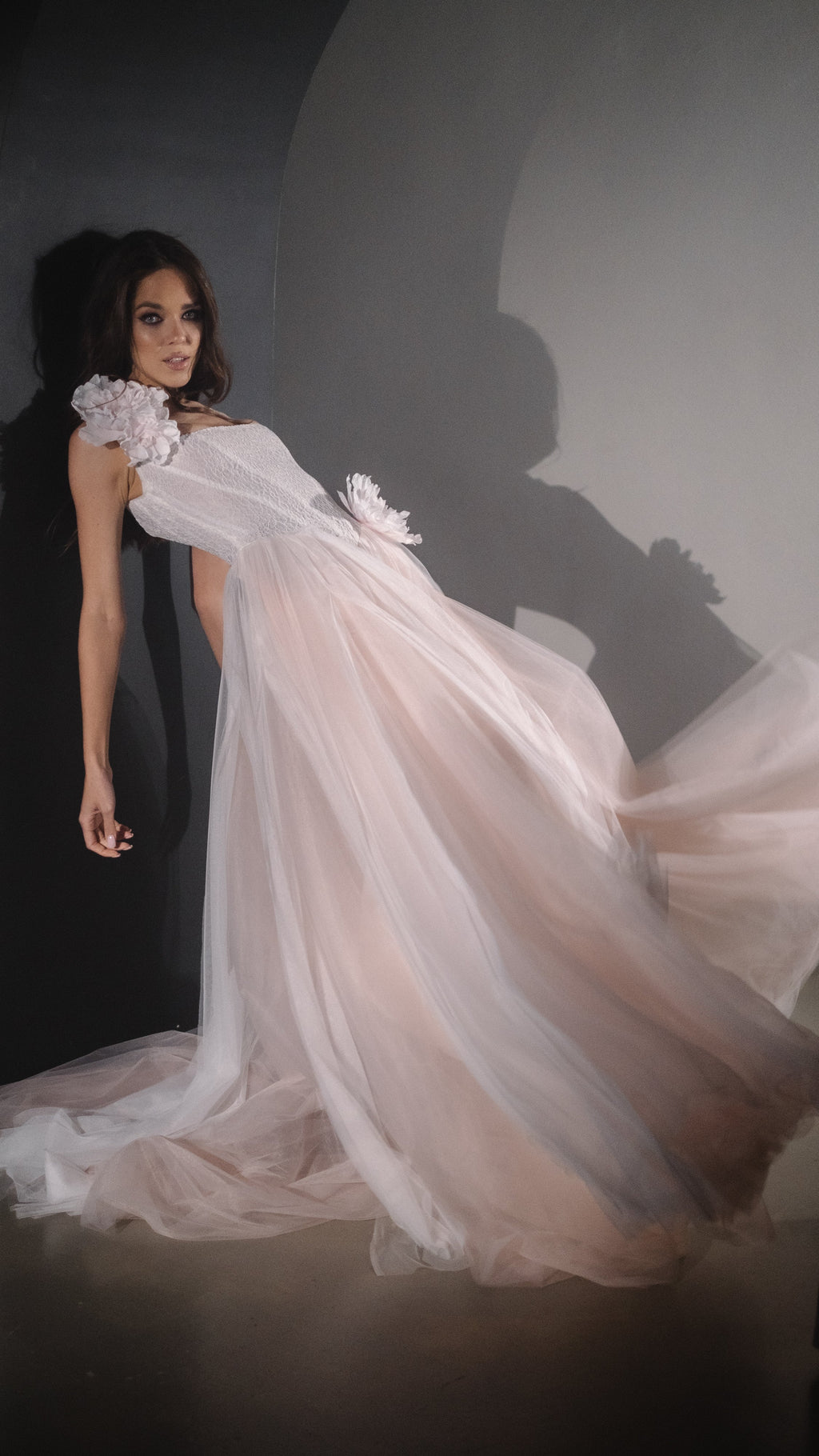 Model leaning back against a wall, blush tulle skirt of a corset wedding dress sweeping out across the floor, Chrysanthemum