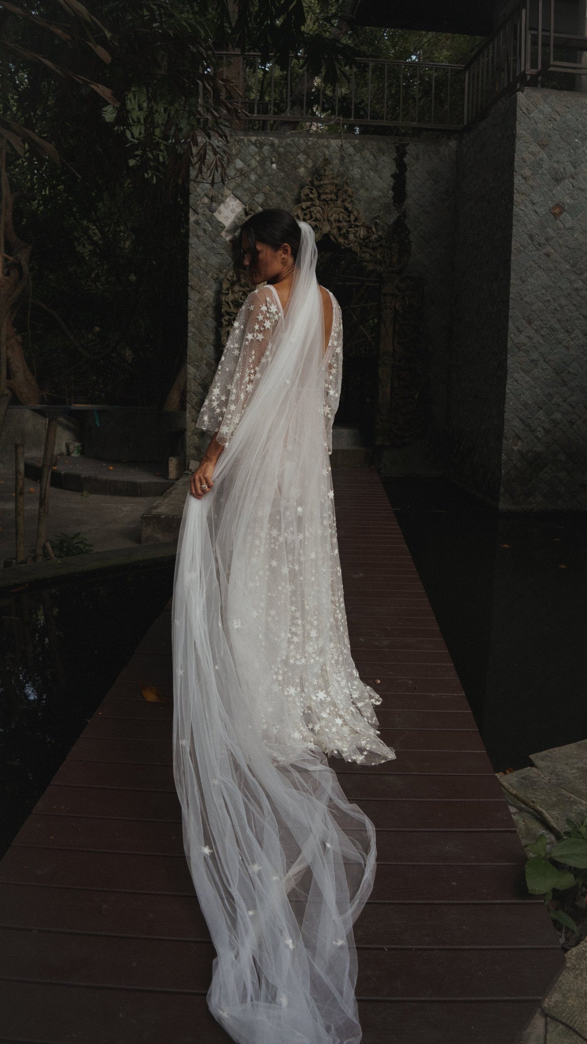 Back view of a cathedral star wedding veil trailing along a wooden boardwalk in a dark garden, star lace gown, Coastal Moonlight Veil