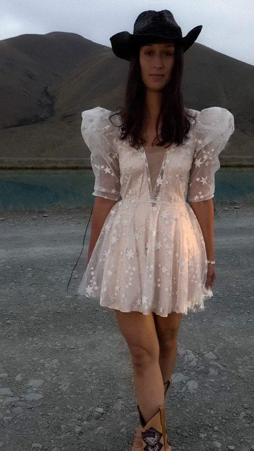 Bride in a black cowboy hat and boots wearing a star lace mini wedding dress with puff sleeves by a lake, Cosmic Dancer