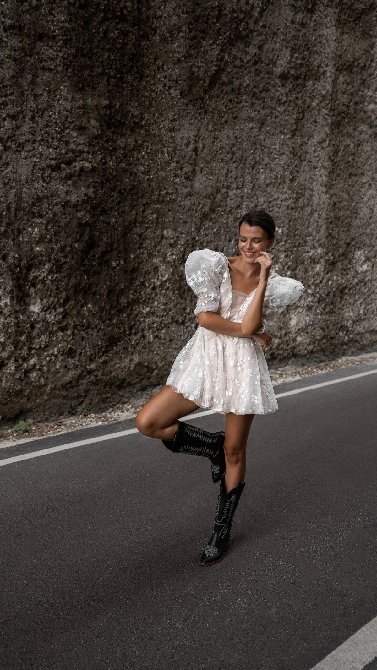Bride balancing on one leg in western boots, short star lace wedding dress with puff sleeves on a roadside, Cosmic Dancer