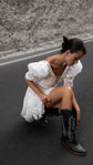 Bride crouched pulling on a black embroidered boot, star lace mini wedding dress with puff sleeves, road shoot, Cosmic Dancer