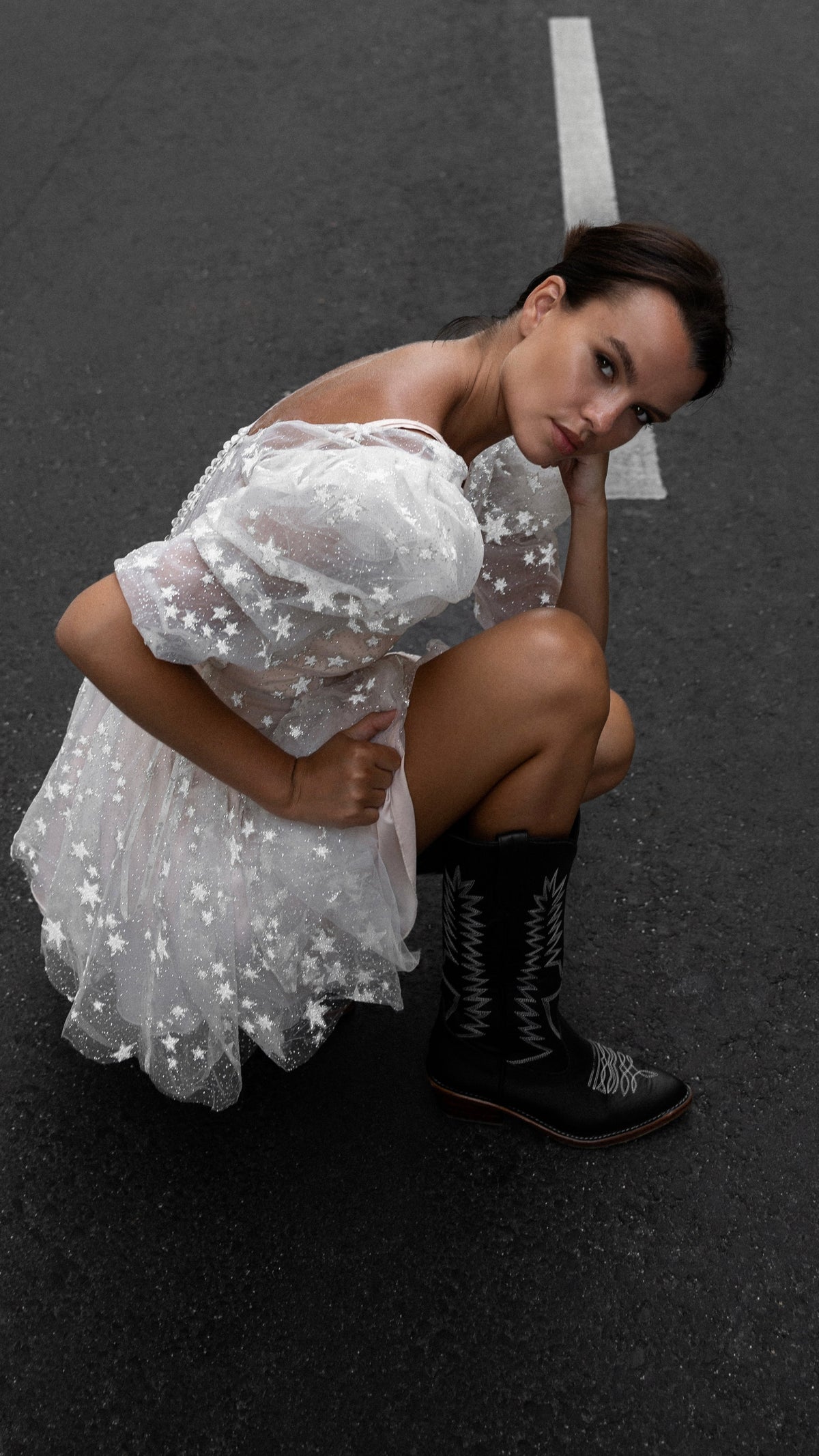 Close crop of a crouching bride in a short starry wedding dress with sheer puff sleeves and black boots, Cosmic Dancer