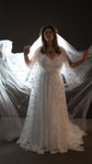 Celestial wedding dress in star lace with sheer flutter sleeves, bride holding a long tulle veil out wide against a dark studio. Counting Stars 2.0 by Ephemeris