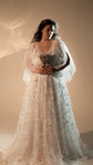 Bride holding a dried protea in front of a star lace wedding dress with sheer flutter sleeves, studio, Counting Stars 2.0