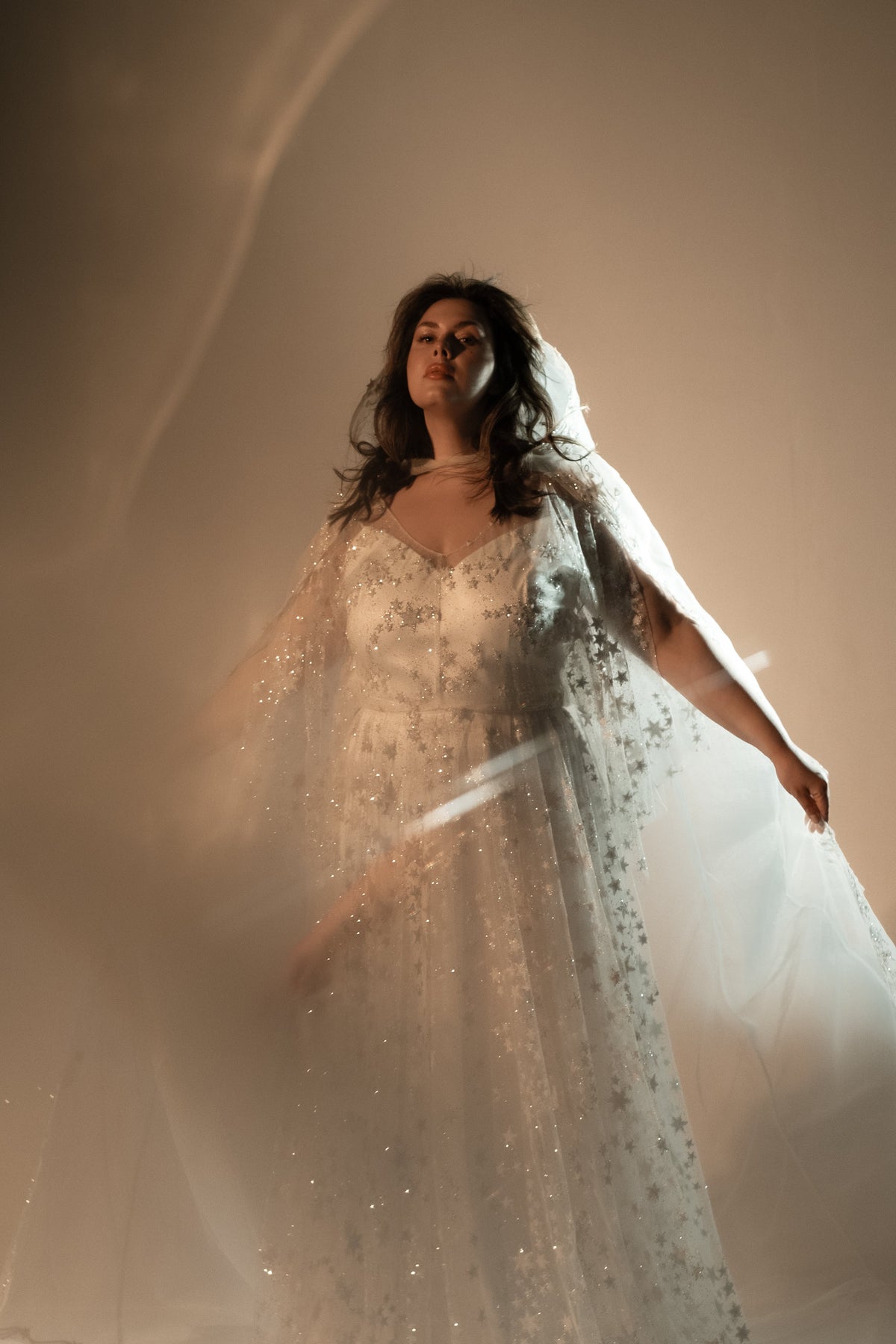 Bride with arm outstretched in a backlit star lace wedding dress and a sheer veil, light streaks behind, Counting Stars 2.0