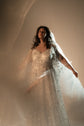 Bride with arm outstretched in a backlit star lace wedding dress and a sheer veil, light streaks behind, Counting Stars 2.0