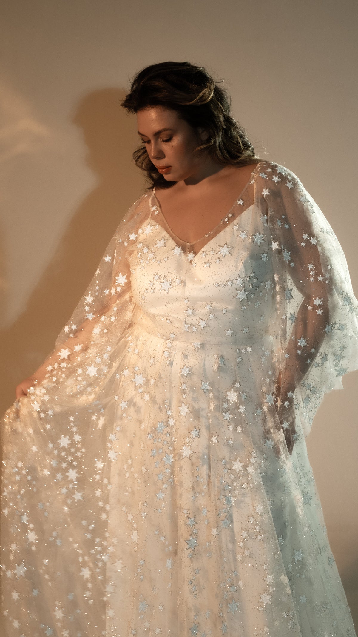 Bride gathering the sheer skirt of a star lace wedding dress, satin slip visible under thin straps, Counting Stars 2.0