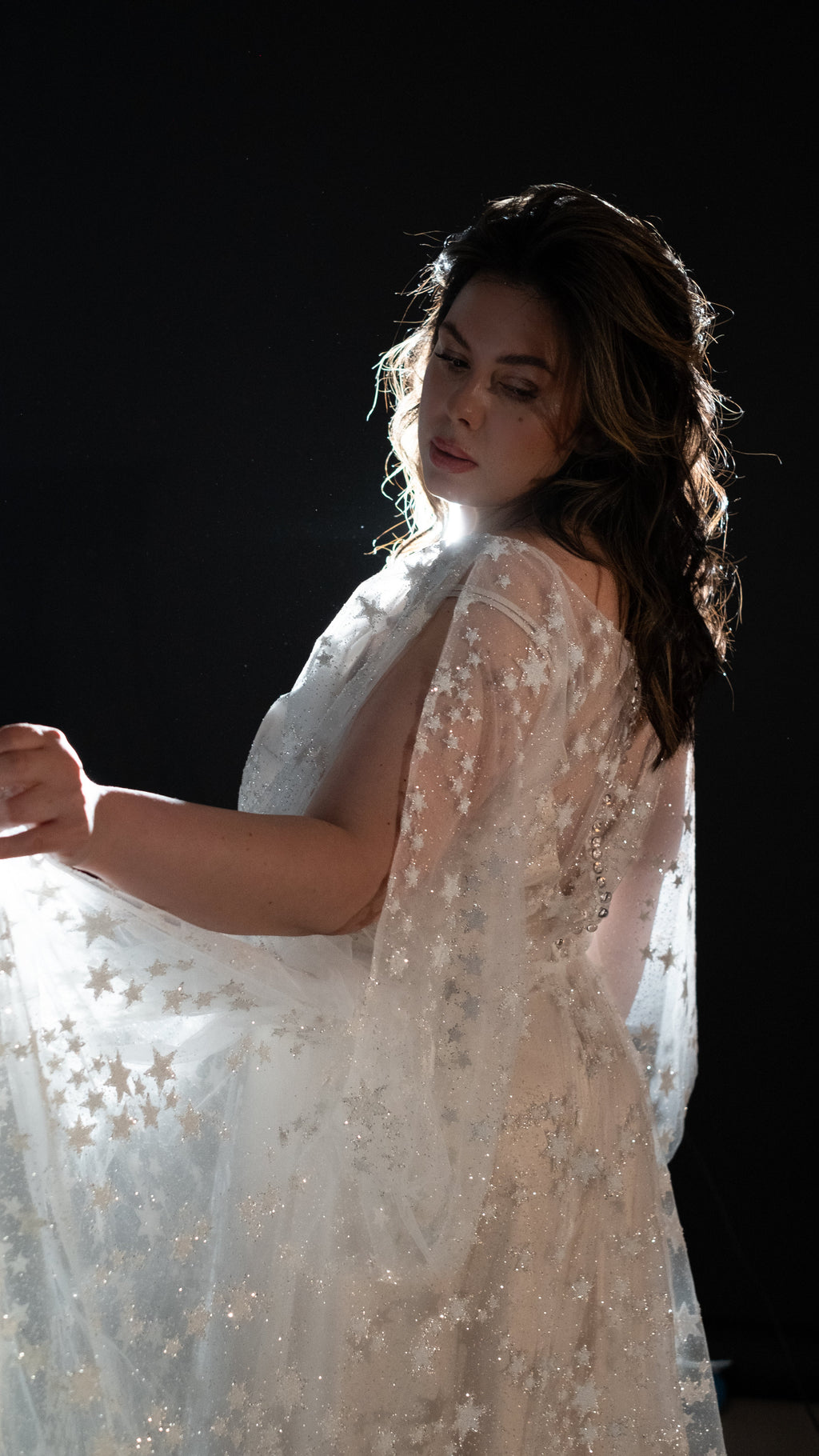 Side view of a bride against a black backdrop, backlit star lace sleeve of a wedding dress glowing, Counting Stars 2.0
