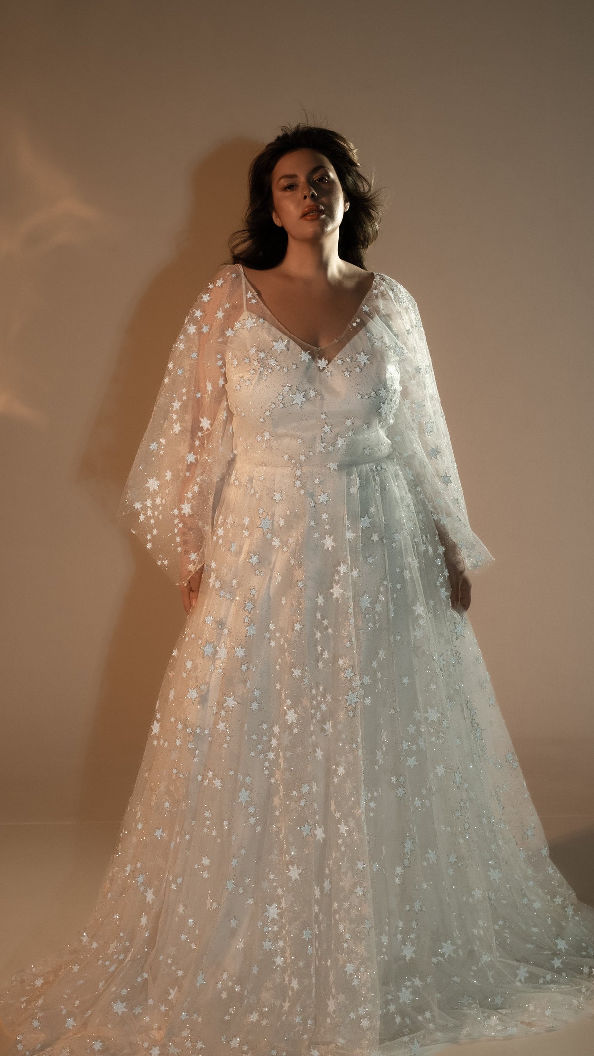 Full-length view of a star lace wedding dress with sheer balloon sleeves and a deep V-neck, beige studio, Counting Stars 2.0