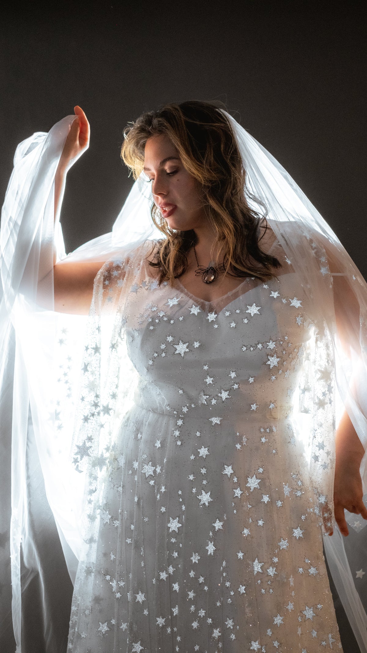 Bride raising a backlit tulle veil above her head, reflective stars glinting on a lace wedding dress, Counting Stars 2.0