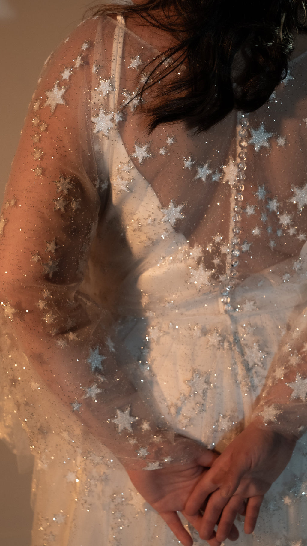 Close-up of hands clasped at the back, translucent buttons and stars on a sheer lace wedding dress, Counting Stars 2.0