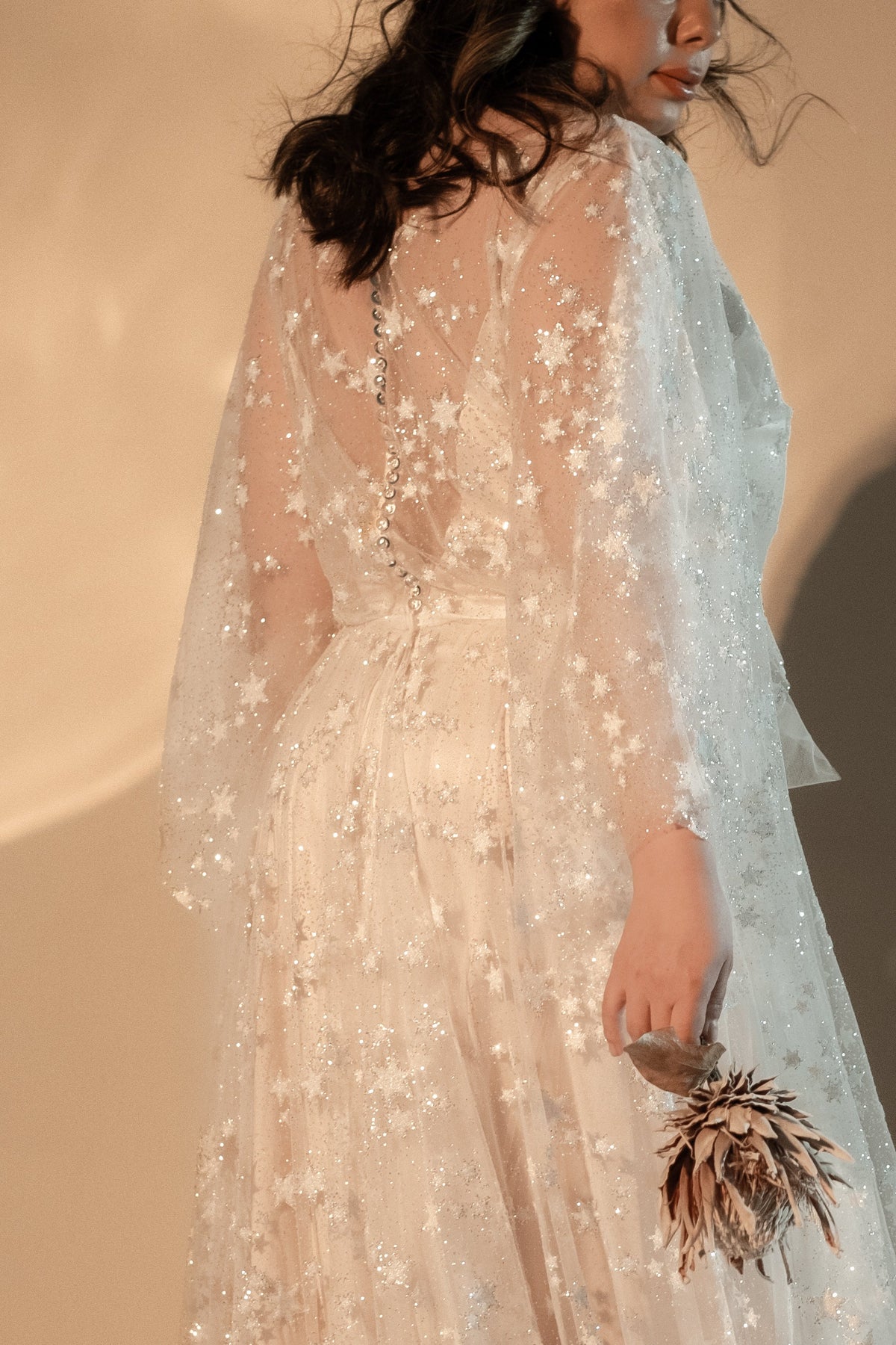 Back view of a star lace wedding dress with a row of translucent buttons and a dried protea in hand, Counting Stars 2.0