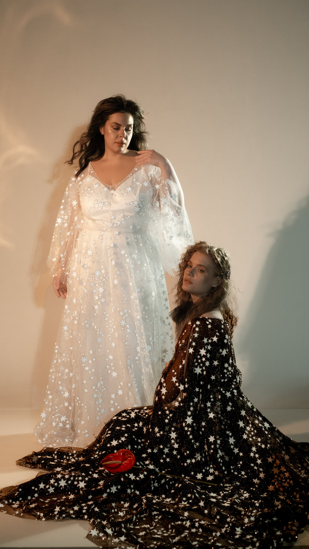 Ivory and black star lace wedding dresses together, one bride standing and one seated, Counting Stars collection