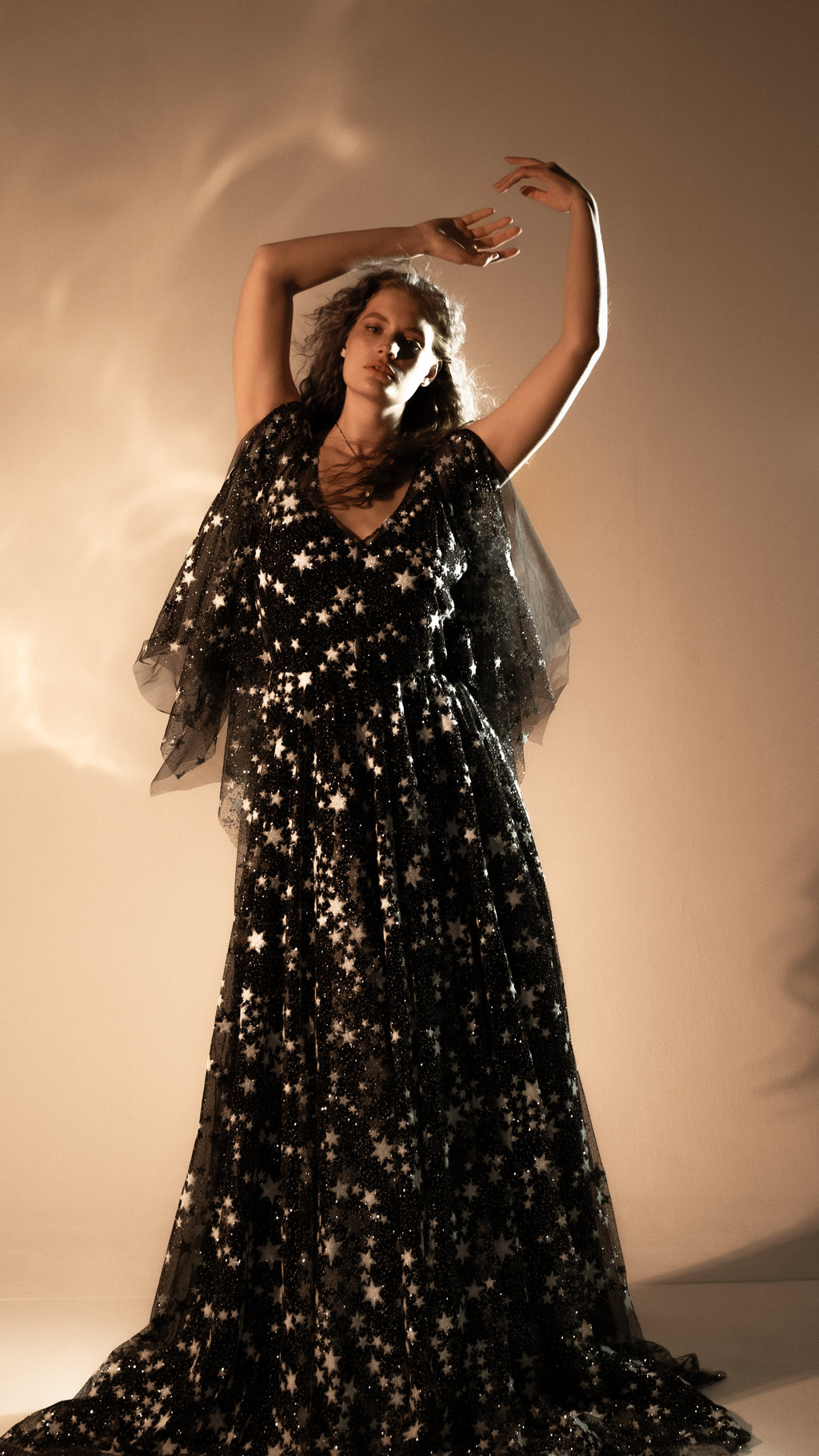 Bride with arms raised in a black star lace wedding gown, sheer flutter sleeves and long tulle skirt, Counting Stars Black