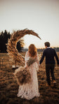 Couple walking toward a pampas grass moon arch at sunset, bride in a star lace wedding dress, Counting Stars Sample