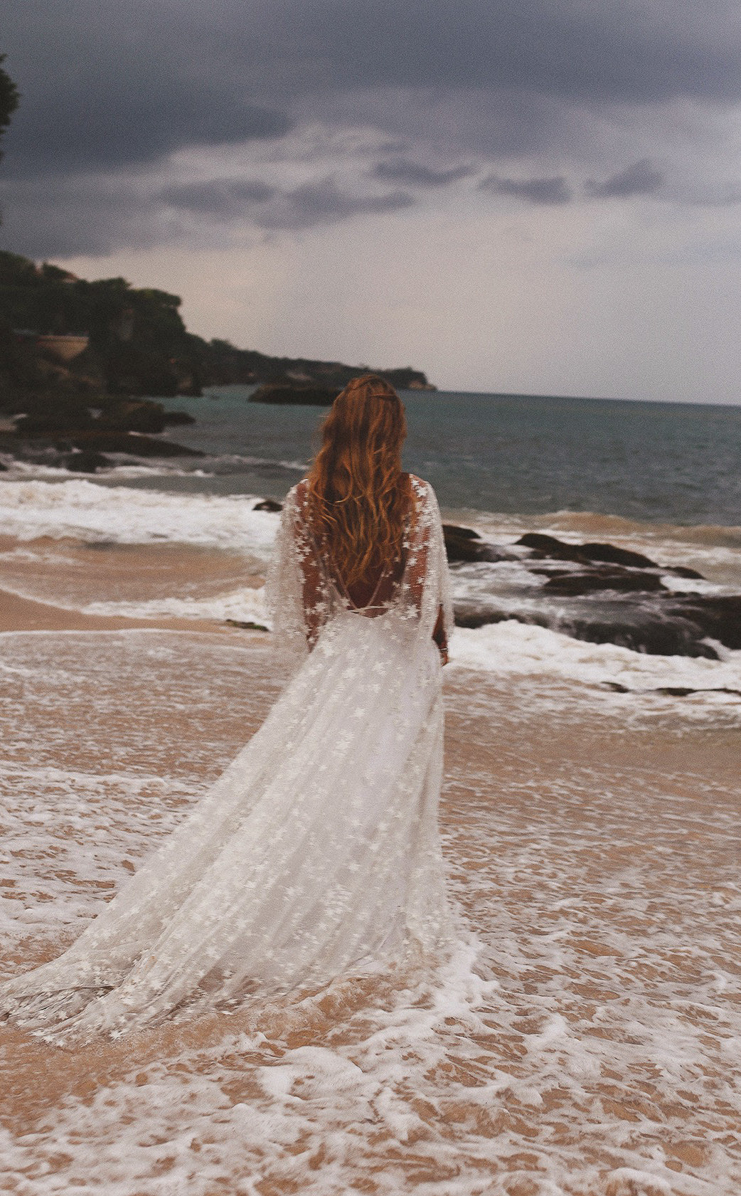 Back view of a bride stepping into the waves, open back star lace wedding dress with a train on wet sand, Counting Stars Sample