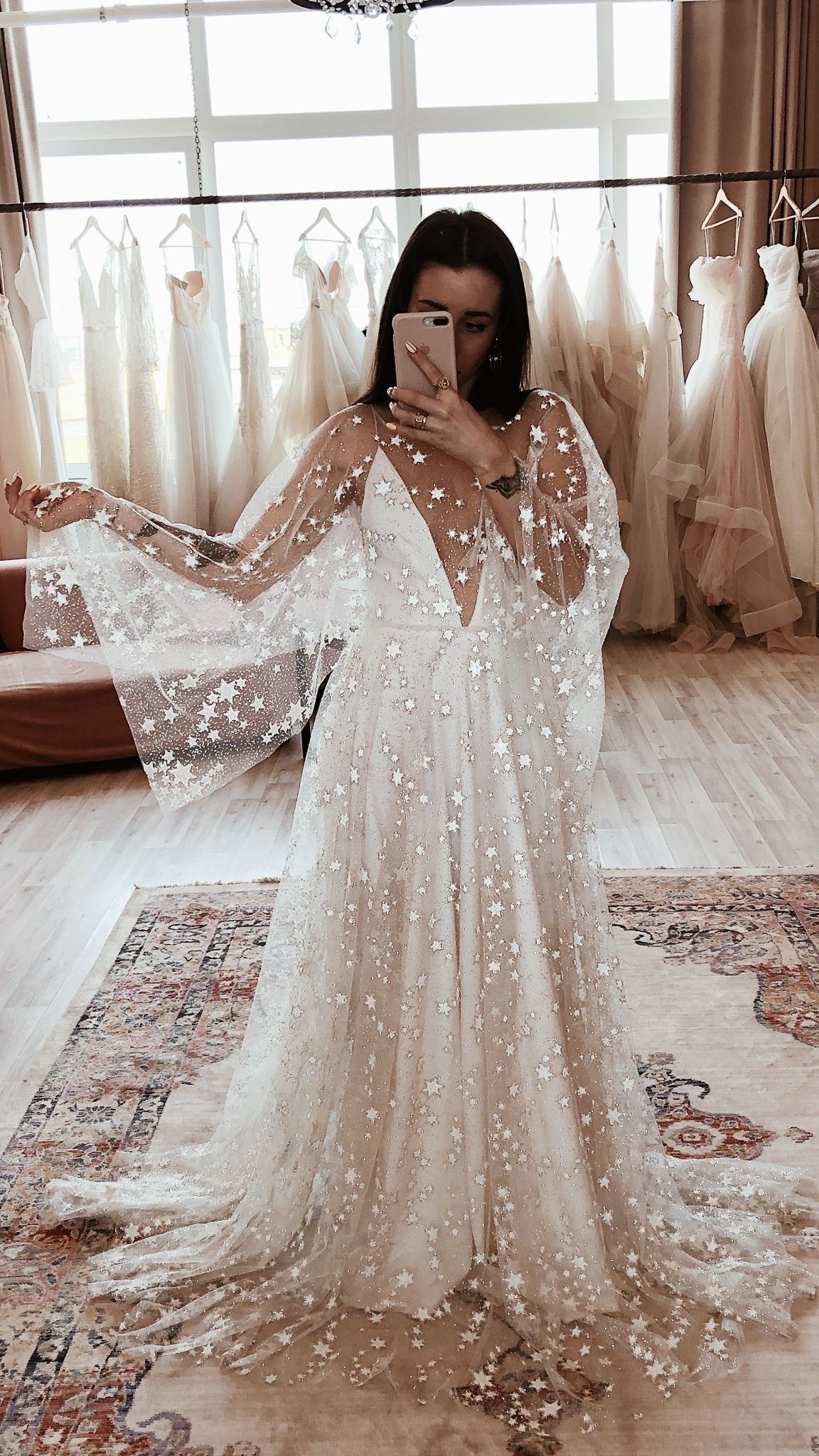 Mirror selfie in a bridal boutique, star lace wedding dress with sheer cape sleeves over a V-neck slip and long train, Counting Stars Sample