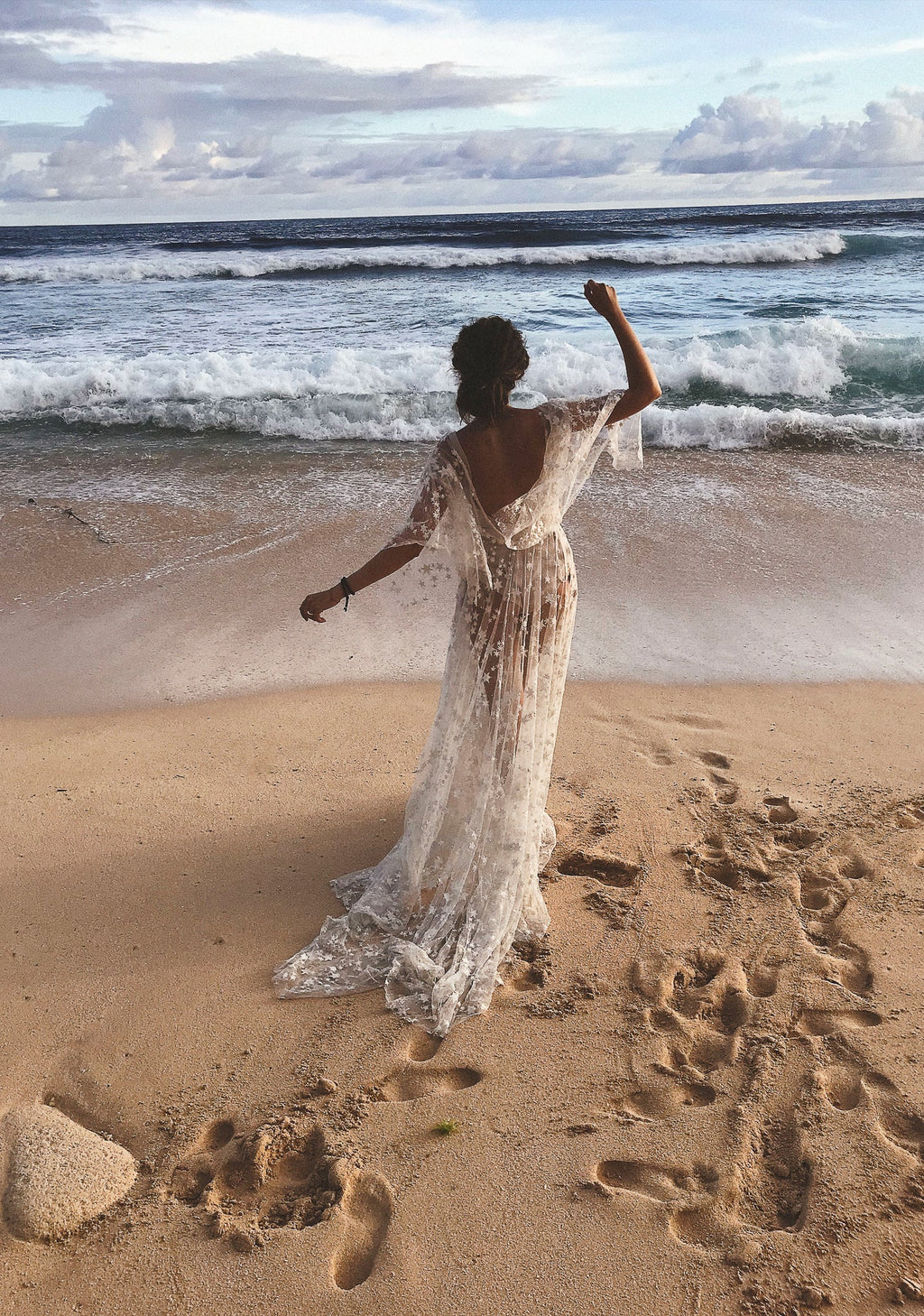 Back view of a bride on a sandy beach raising one arm, open back star lace wedding dress by the waves, Counting Stars Sample