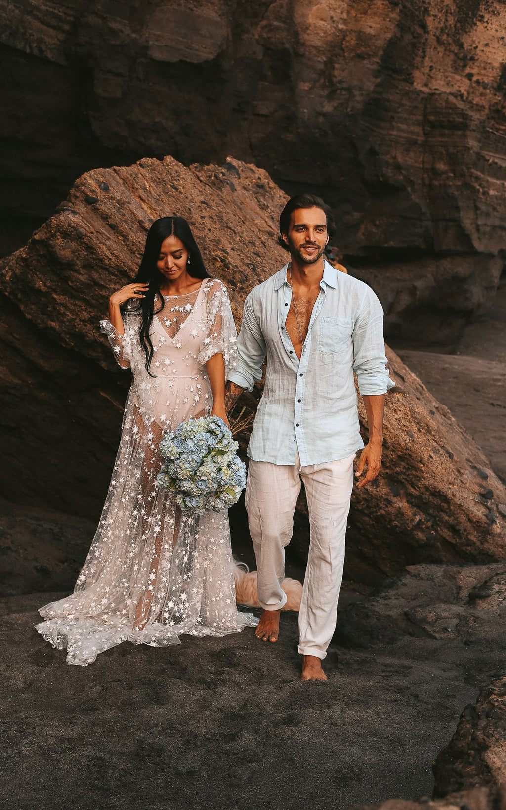 Couple walking on a rocky beach, bride in a sheer star lace wedding dress with blue hydrangeas, Counting Stars Sample