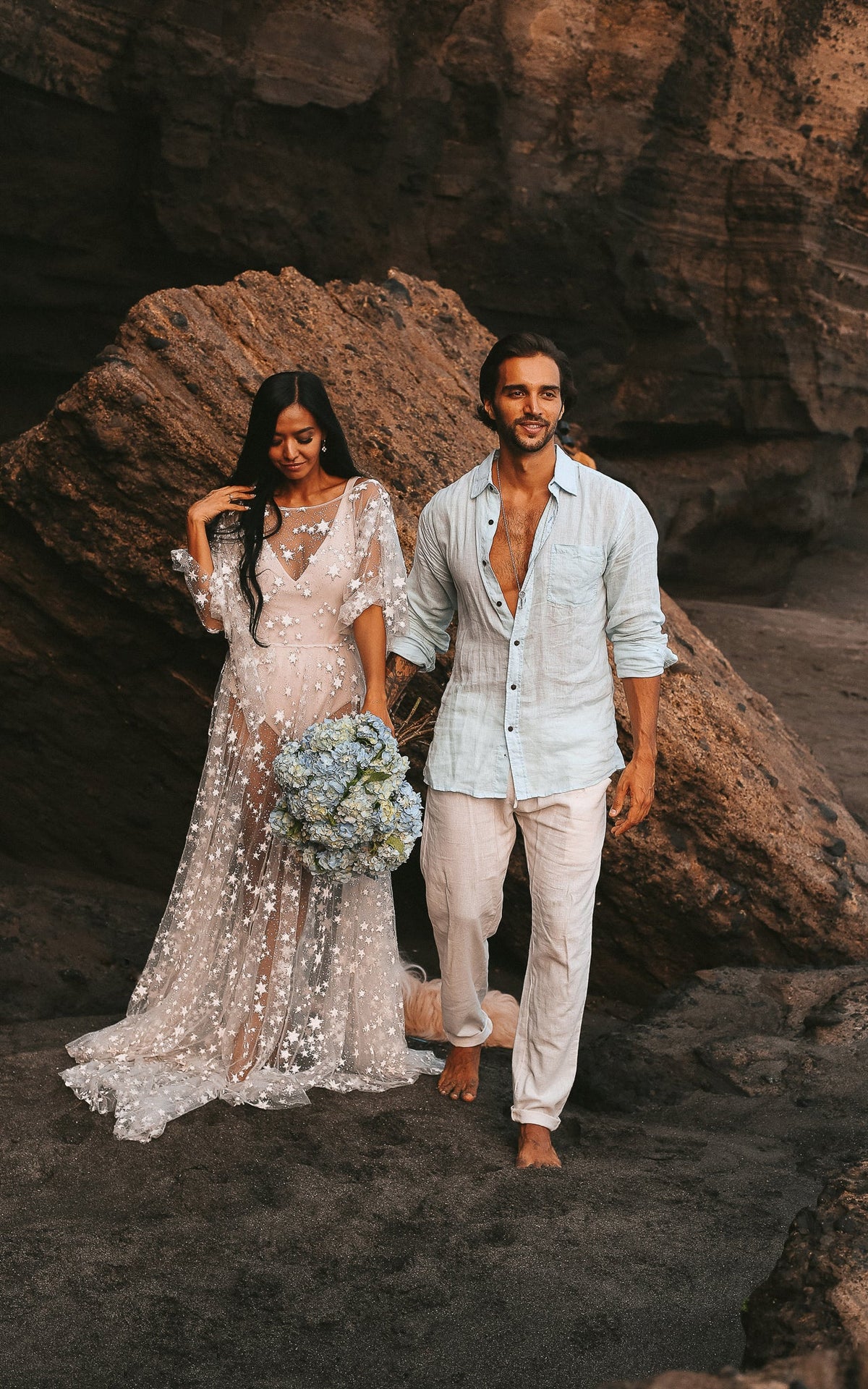 Couple walking on a rocky beach, bride in a sheer star lace wedding dress with blue hydrangeas, Counting Stars Sample
