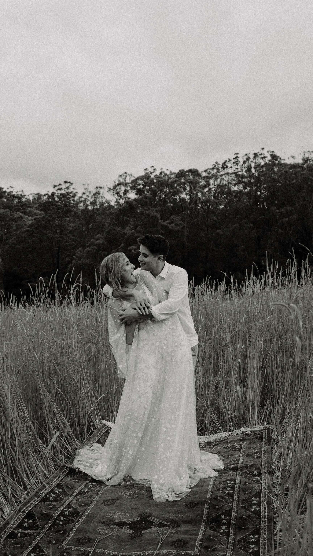 Black and white shot of a couple in tall grass on a rug, bride in a long star lace wedding dress, Counting Stars Sample