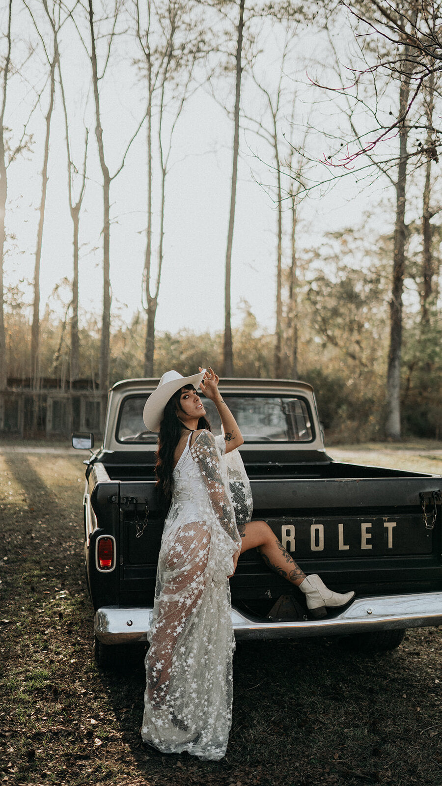 Bride resting one boot on a pickup tailgate in a cowboy hat, sheer star lace wedding dress, Counting Stars Sample