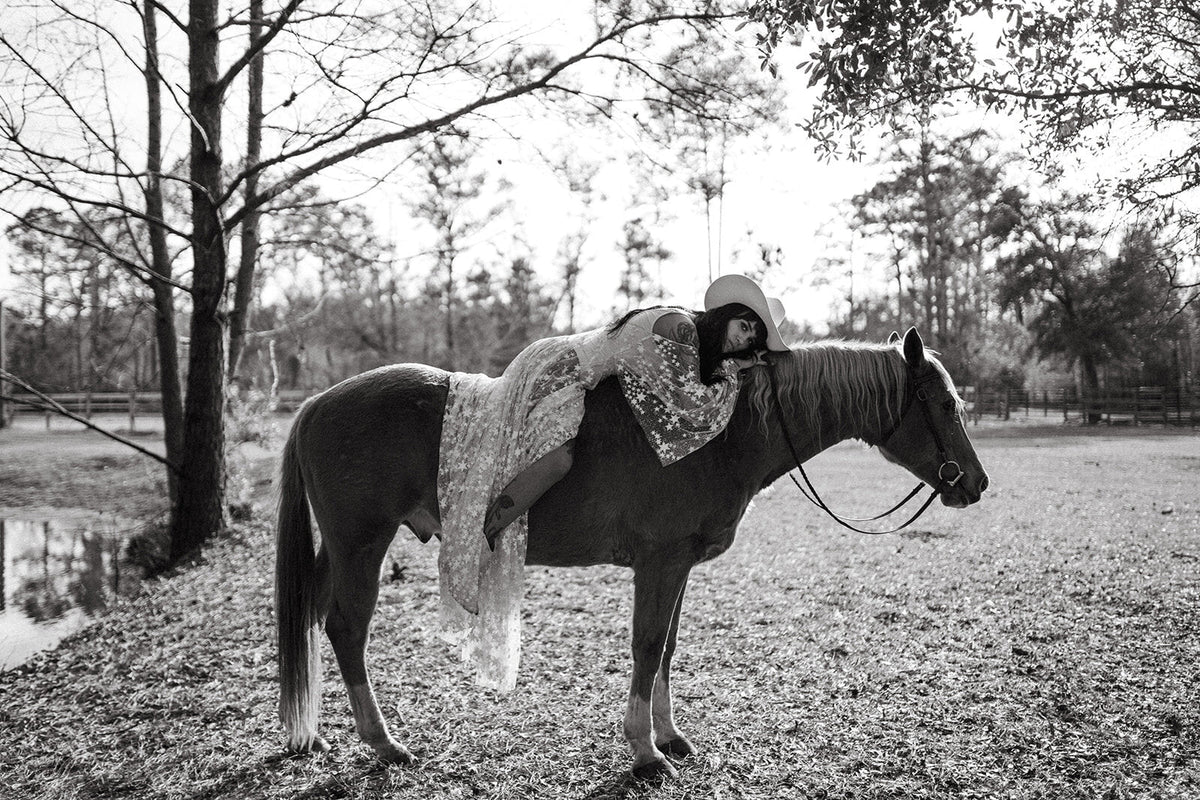 Black and white image of a bride lying back across a horse, star lace wedding dress hanging down, Counting Stars Sample