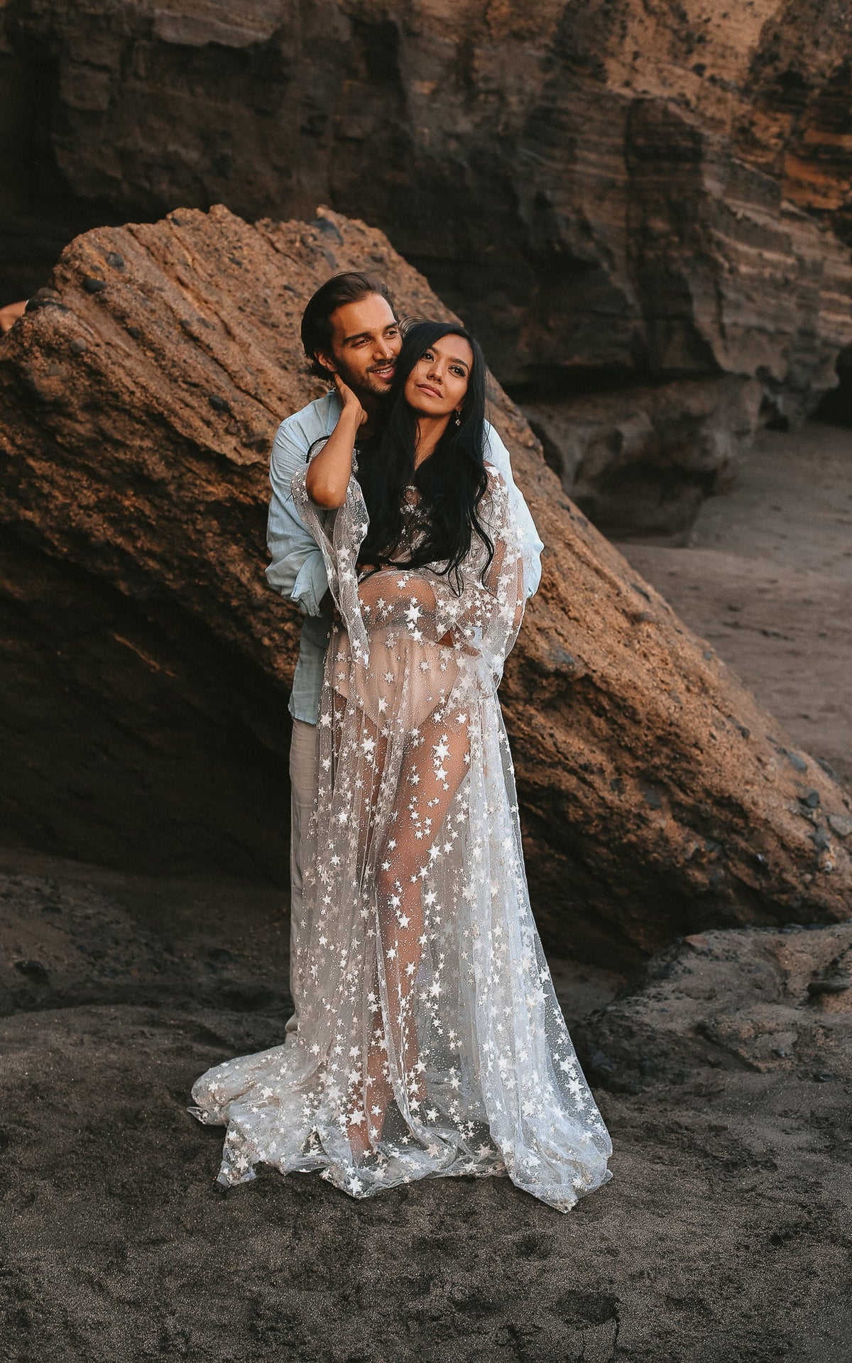 Couple embracing against a red rock, bride in a sheer star lace wedding dress with puff sleeves, Counting Stars Sample