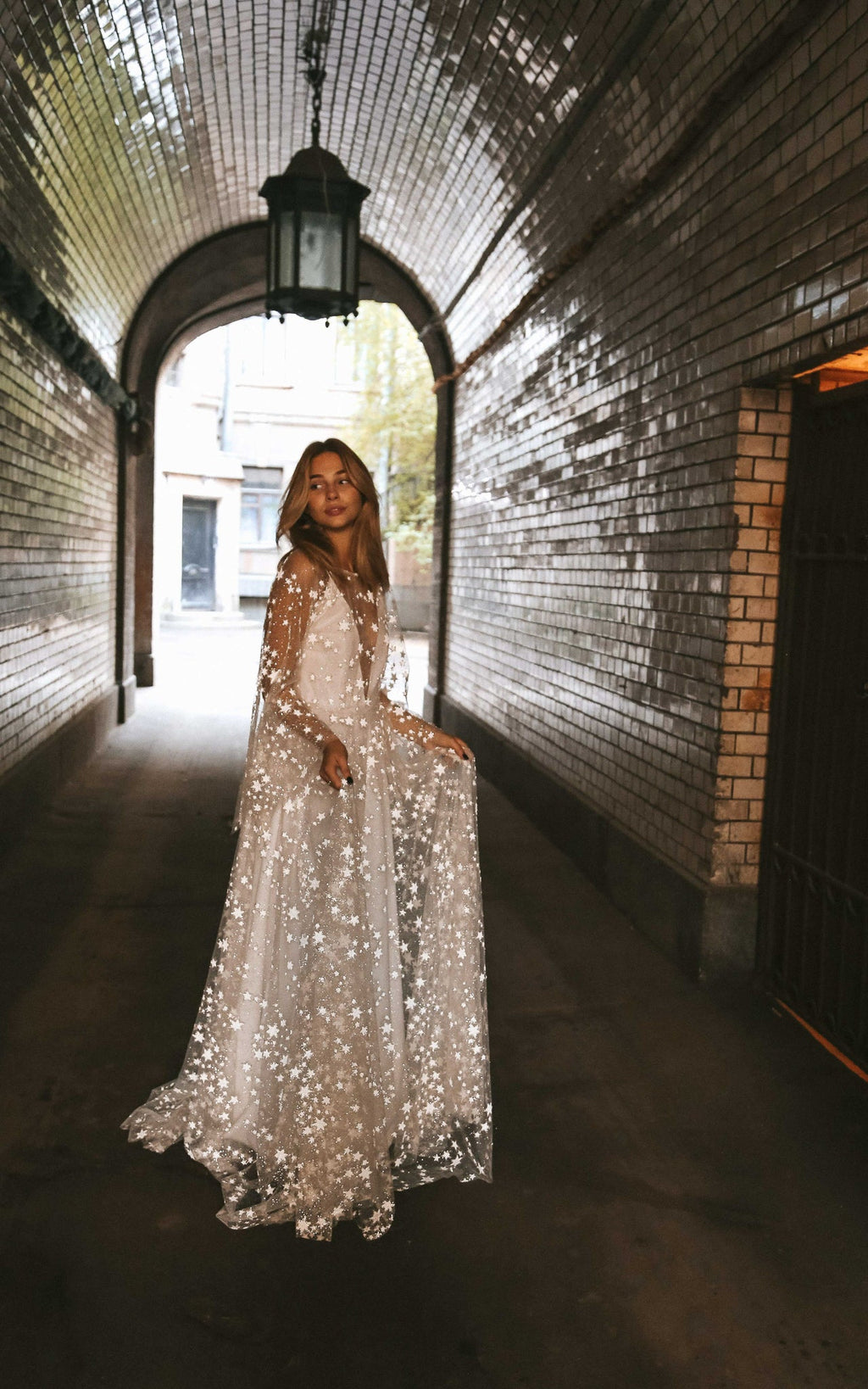 Full-length star lace wedding dress with long sleeves in a brick tunnel under a hanging lantern, Counting Stars