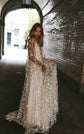 Bride holding out the skirt of a long sleeve star lace wedding dress in a tiled archway, Counting Stars