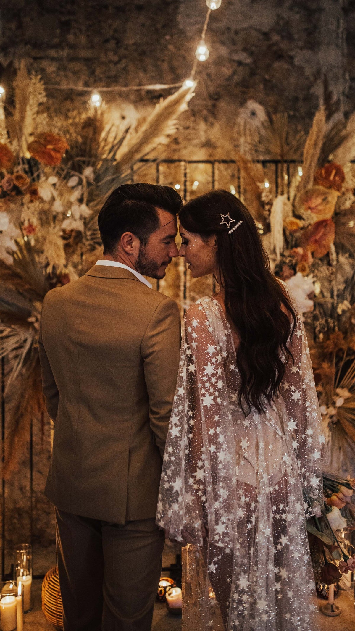 Couple touching foreheads by a dried flower arch, bride in a star lace wedding dress with cape sleeves, Counting Stars