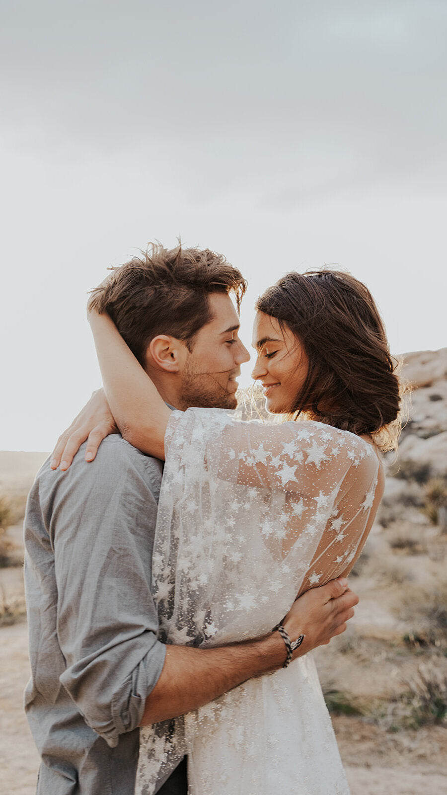 Couple embracing in the desert, bride in a starry lace wedding dress with sheer flutter sleeves, Counting Stars