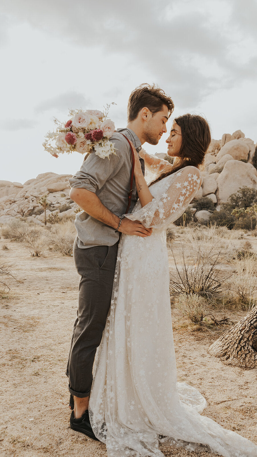 Groom kissing the bride in the desert, long star lace wedding dress and train, bouquet raised high, Counting Stars