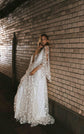 Bride leaning on a brick wall at night in a star lace wedding dress with long cape sleeves and a soft train, Counting Stars