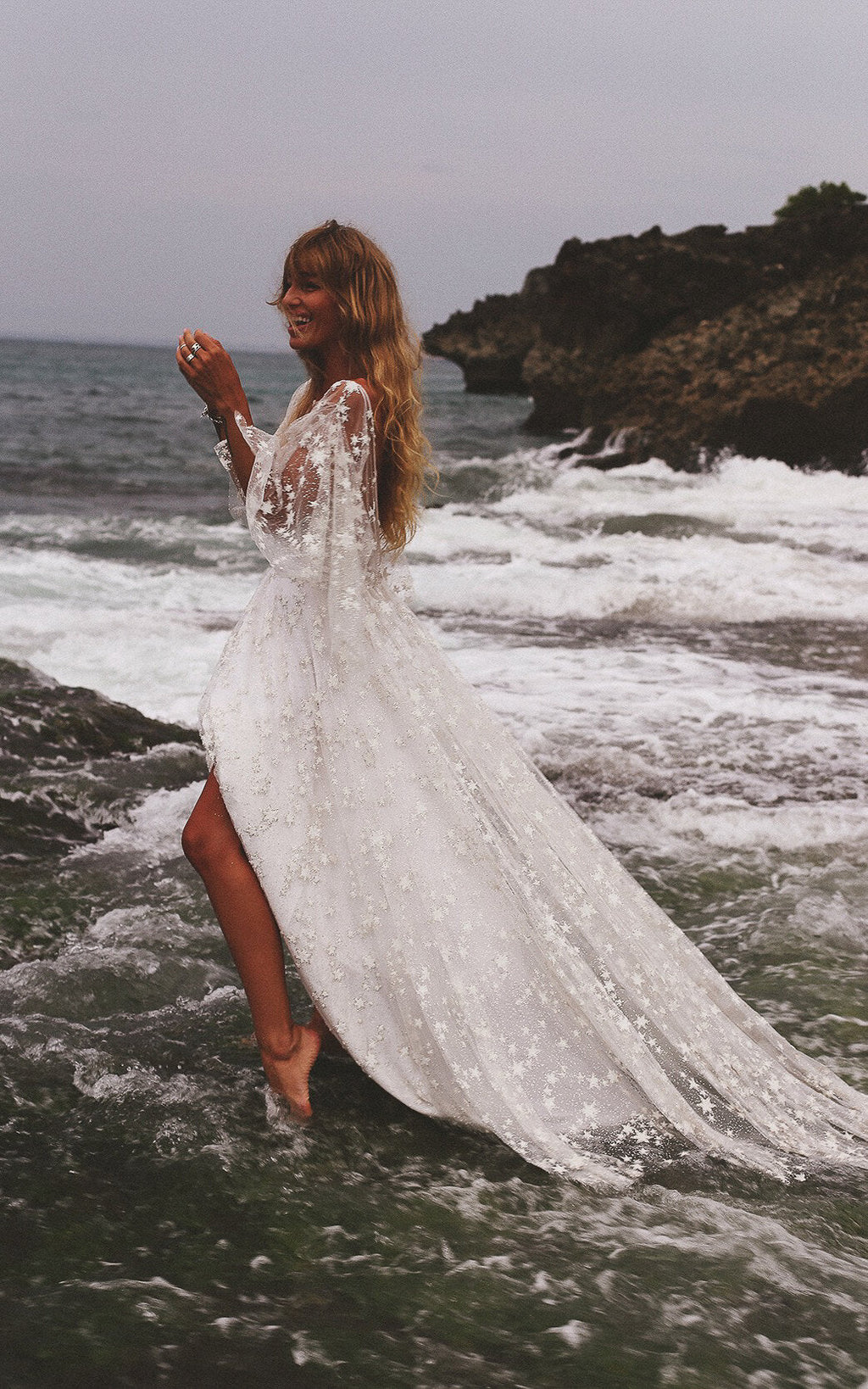 Bride wading into the sea, star lace wedding dress with long sleeves and a high slit soaked by the waves, Counting Stars