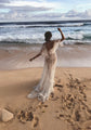 Back view of a bride on the sand with one arm up, open back star lace wedding dress and waves rolling in, Counting Stars