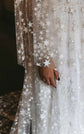 Close-up of starry lace on a sheer sleeve and skirt, glittering stars over a satin slip, Counting Stars wedding dress