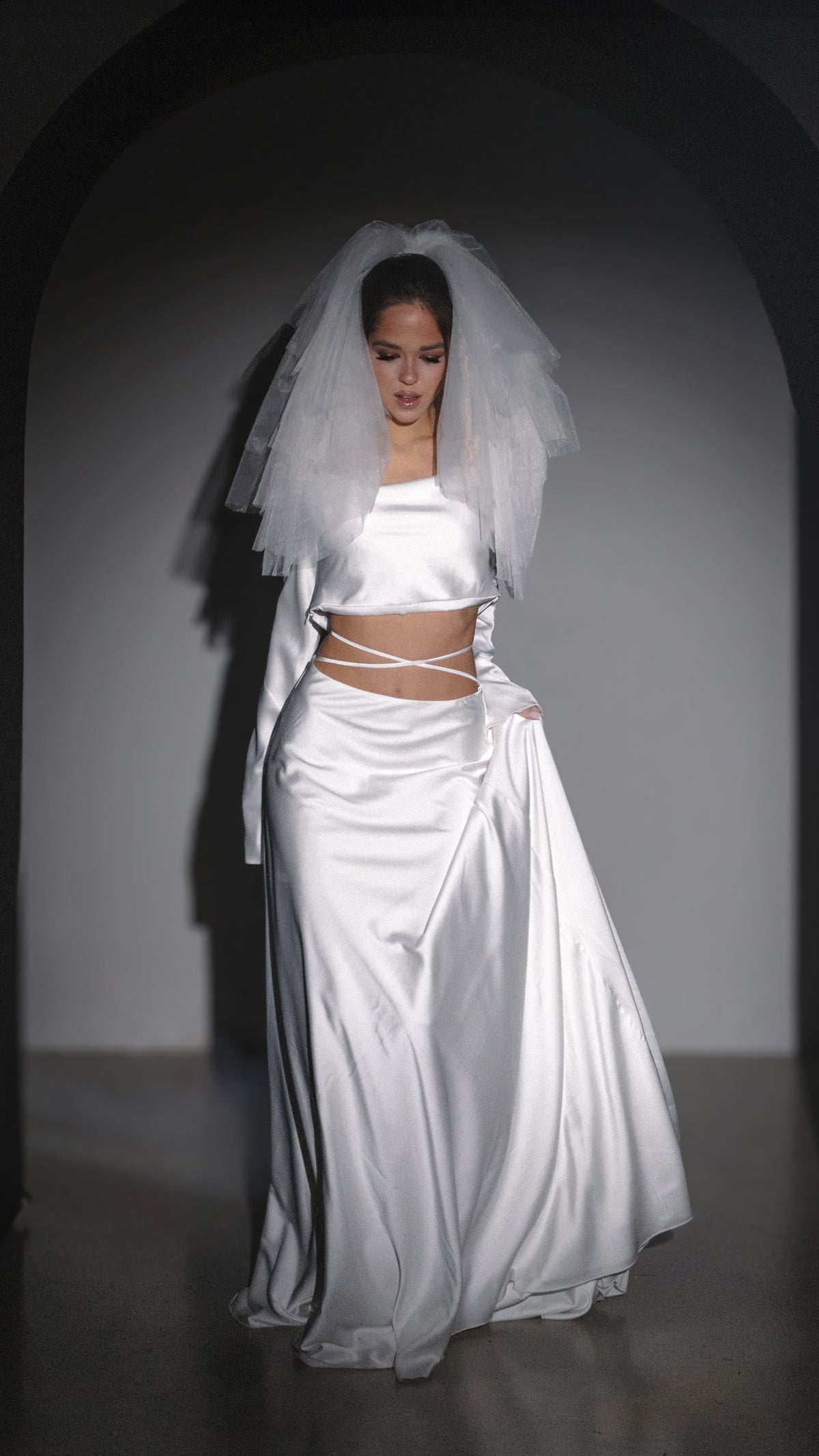 Two-piece silk satin wedding dress, long sleeve crop top and bias skirt with crossed waist ties, short tulle veil, studio arch. Danielle by Ephemeris