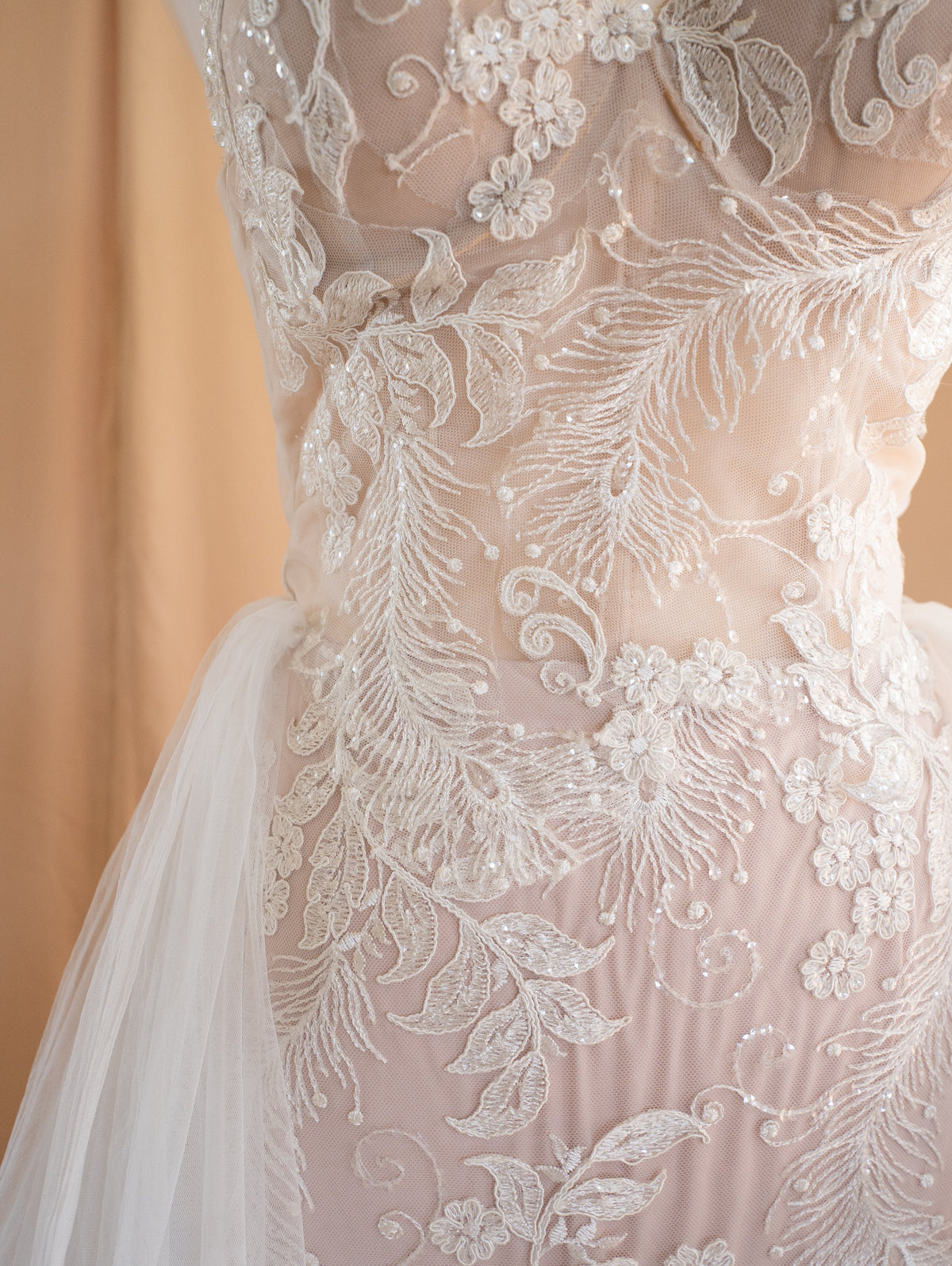 Close-up of feather and leaf corded lace appliques over a beige lining on a fitted wedding dress, Feathers Sample