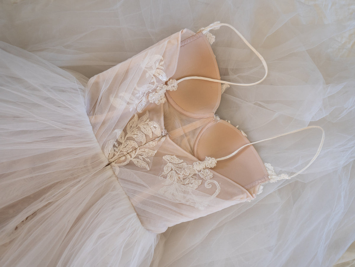 Flat lay detail of a lace wedding dress bodice with structured cups and thin straps on tulle, Feathers Sample