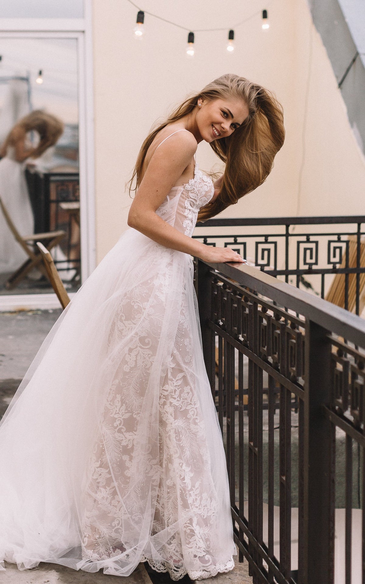Bride smiling and leaning on a balcony rail, side view of a lace wedding dress with a long tulle skirt, Feathers Sample