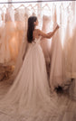 Back view of a bride touching gowns on a rail, strappy back of a wedding dress and a tulle train, Feathers Sample